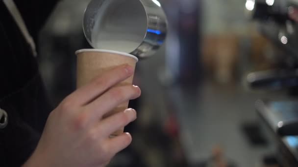 Mãos masculinas barista despeje leite espumado em um copo descartável cheio de café preto. O processo de fazer cappuccino — Vídeo de Stock
