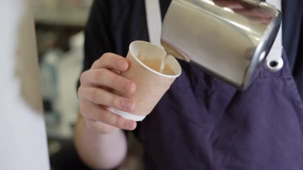 Großaufnahme von männlichen Händen, die gedämpfte Milch in Einweg-Pappbecher gießen, während sie Latte-Art-Kaffee zubereiten. Zubereitung von frischem Cappuccino. Zubereitungskonzept, Morgenkaffee. — Stockvideo