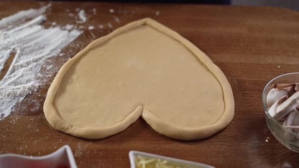 Kochen herzförmige Pizza zum Valentinstag für einen geliebten Menschen. Tomatensauce auf den Teig gießen. 4K-Video — Stockvideo