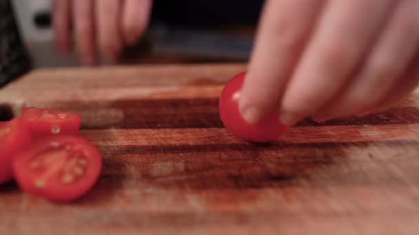 Lo chef prende i pomodorini, taglia la verdura a metà con un coltello da cucina su un tagliere di legno. Primo piano. — Video Stock