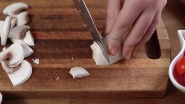 Ženské ruce krájely houby kuchyňským nožem na dřevěné řezací desce, zblízka. Champignone. žena připravuje večeři doma — Stock video