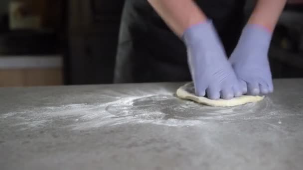 Un chef de pizza italiano forma una masa sobre una superficie enharinada y la amasa con las manos en una cocina tradicional de pizzería. primer plano de las manos con guantes — Vídeos de Stock