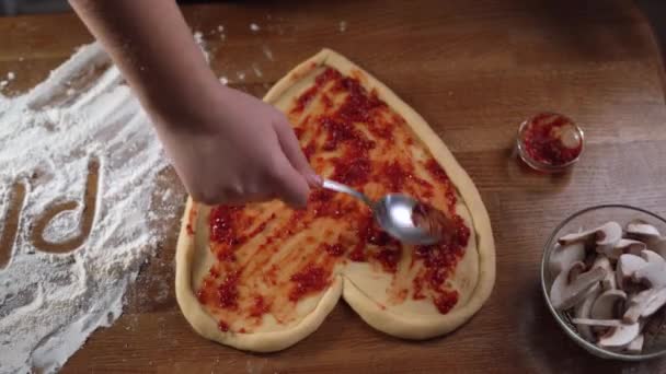 Gotowanie pizzy w kształcie serca na Walentynki dla ukochanej osoby. Wylać sos pomidorowy na ciasto. Wideo 4K — Wideo stockowe