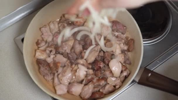 Шматочки свинини смажать на сковороді в рослинній олії, жіноча рука кидає подрібнену цибулю . — стокове відео