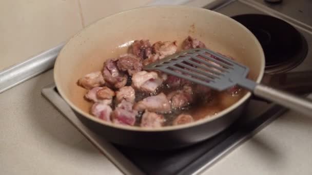 La carne cortada en trozos se mezcla con una espátula y se fríe en una sartén en aceite. Concepto de alimentos poco saludables. — Vídeos de Stock