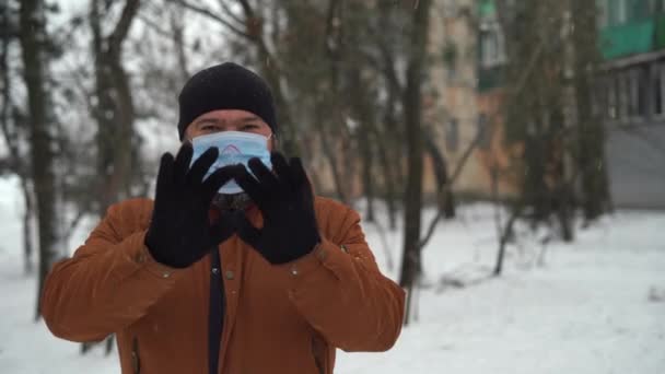 人は雪の間の冬に指から愛の心を作る。顔に医療マスク。愛の記号. — ストック動画