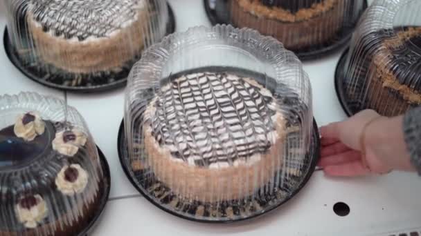 Vitrine avec de délicieux gâteaux emballés dans des récipients en plastique transparent dans un supermarché close-up. Femme main prend une boîte avec dessert — Video