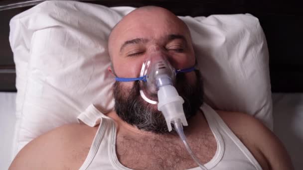 Na posteli leží vousatý muž s kyslíkovou maskou a umělou plicní ventilací. Otevře oči. Koncept pacienta se měl uzdravit. — Stock video