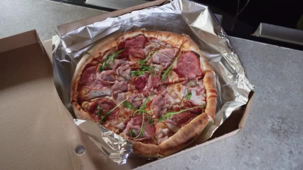 Lezzetli ve iştah açıcı taze pizzanın kutuda üst görüntüsü, erkek elleri kapağı kapatır. Salgın sırasında paket yemek ve pizza teslimatı konsepti — Stok video