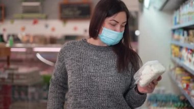 Koruyucu tıbbi maske takan bir kadın süpermarketten ya da marketten yiyecek alır. Müşteri süt ürünlerini ve süzme peyniri sepete koyar.