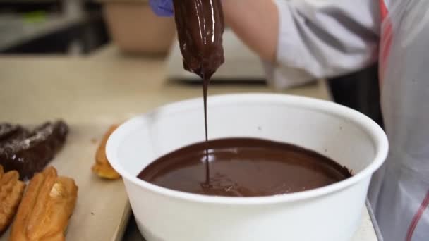 Een vrouwenhand dompelt een eclair in zoete chocolade, close-up, — Stockvideo