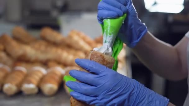 Una donna riempie le corna di crema da una borsa da pasticceria. Mani in alto i guanti — Video Stock