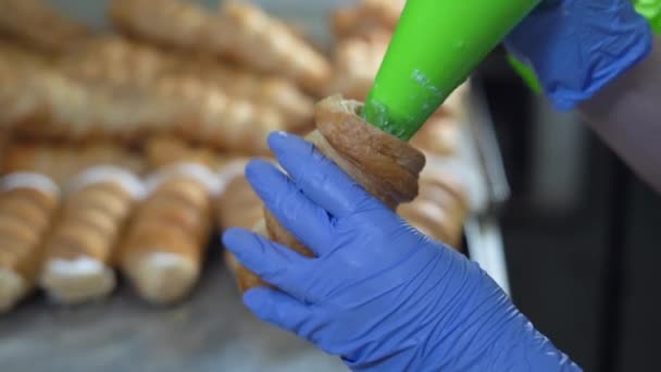 Une femme remplit les cornes de crème d'un sac à pâtisserie. Mains dans les gants gros plan — Video
