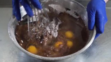 Büyük bir kasede çikolatalı kek hamuru pişiren şef, onları çırpıcıyla karıştırmaya başlar.