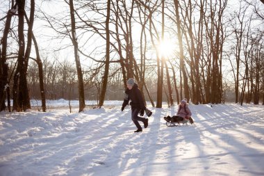 Mutlu çocuk, soğuk bir kış gününde, kızakla bir kızı dışarı çeker. Harika bir akşam güneşi. Boşluğu kopyala