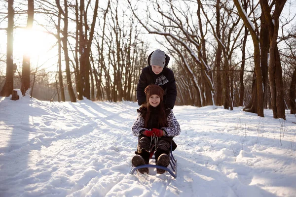 Boy and girl enjoying a sleigh ride. Push the sled and have fun. Children play outside in the snow. — Stock Photo, Image