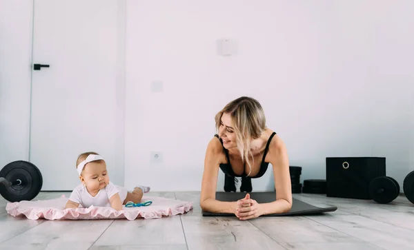Happy mom and daughter on the floor in the room doing exercises on the gymnastic rug at home. Fitness and recovery concept after childbirth.