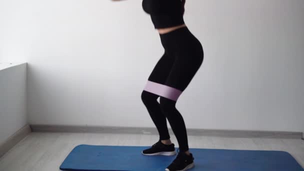Sportive sportive girl doing fitness aerobic exercises against a white wall background. Elastic squats. Home workout, — Vídeo de stock