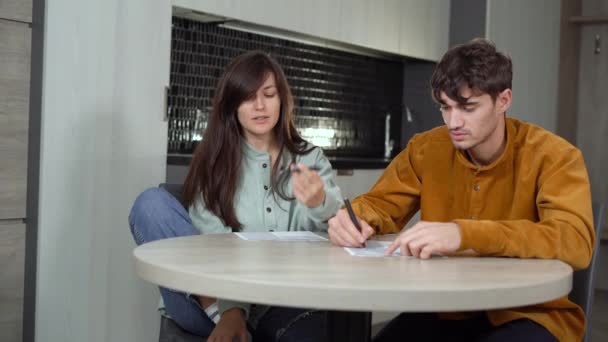 Una pareja joven de cónyuges está sentada en una mesa en la cocina y calculando los gastos y los ingresos de la familia. Mantenimiento de registros para mantener la estabilidad financiera. — Vídeo de stock