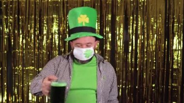 Sakallı sarhoş adam Aziz Patrick gününü kutluyor, elinde bir bardak yeşil bira ve sendeleyici tutuyor. Kostüm partisi. Uzayı kopyala tıbbi yüz maskesi