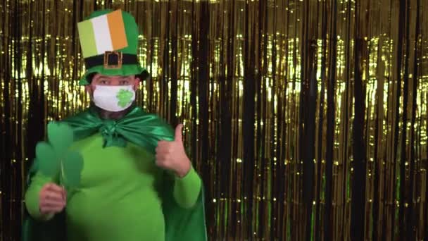 Ein älterer Kobold feiert während der Pandemie den St. Patricks Day, indem er eine medizinische Maske trägt. Der Daumen zeigt auf eine Leerstelle — Stockvideo