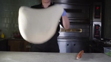 Şef üniformalı genç adam restoranın mutfağına pizza hamuru atıyor..