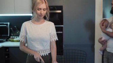 Babası, kızının kollarında mutfakta, annemin yanında. Kadın salata için sebze ve ot kesiyor. Sağlık için diyet.