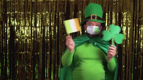 Un giovane folletto celebra il giorno delle stecche durante la pandemia indossando una maschera medica. Contiene una foglia di trifoglio e la bandiera dell'Irlanda. — Video Stock