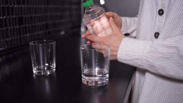 Una mano de mujer toma una botella de plástico y vierte agua en un vaso. — Vídeo de stock