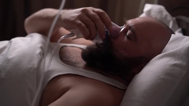 Бородатый больной мужчина лежит на кровати, надевая кислородную маску на лицо. — стоковое видео