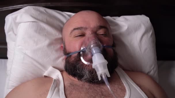 Brodatego chorego leży na łóżku, otwiera oczy i usuwa respirator z twarzy — Wideo stockowe