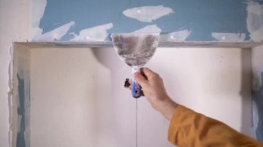 Duvara macun uygulayan bir zanaatkârın elindeki malanın yakın çekimi. Odanın köşesini düzleştirme konsepti