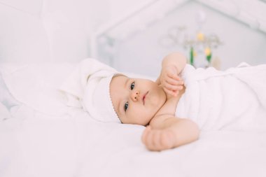6 aylık bir kız, kafasında ve vücudunda havluyla yatakta yatıyor. Hijyen ve bebek bakımı konsepti. Boşluğu kopyala.
