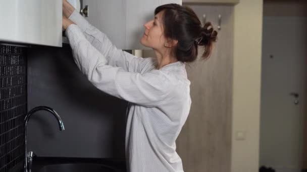 Красивая молодая женщина в мужской рубашке открывает шкаф на кухне, мужчина обнимает и целует ее. — стоковое видео