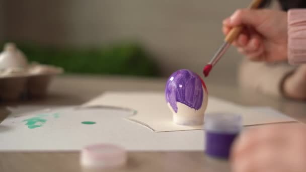 Mãos de uma menina com uma escova nas mãos, que pinta um ovo com tintas acrílicas para o feriado de Páscoa. A criança pinta ovos. — Vídeo de Stock