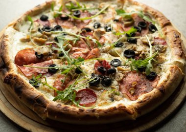 Gri arka planda yuvarlak bir tahta üzerinde peynirli, salamlı ve zeytinli hazır büyük boy pizza. Boşluğu kopyala.