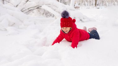 Kırmızı örgü şapkalı ve ceketli küçük mutlu beyaz kız karda tek başına yatıyor. Çocuklar ve soğuk hava için kış eğlencesi. Boşluğu kopyala.