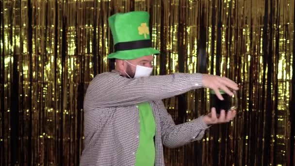 Maschio leprecauno indossa un grande cappello di trifoglio verde e maschera medica che celebra st patricks giorno. beve birra verde attraverso un tubo cocktail. — Video Stock