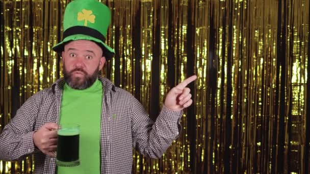 Vit skäggig man som håller ett glas grön öl i handen och pekar med pekfingret mot ett tomt textutrymme. Saint Patricks dag firande koncept. — Stockvideo