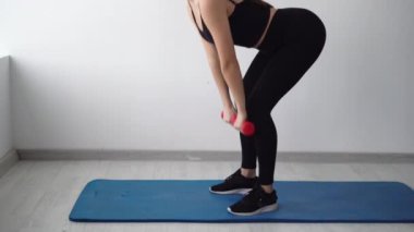 Genç kız dambılı eğiyor, beyaz bir arka planda eğilim gösteriyor, evde spor yapıyor, sağlıklı bir yaşam tarzı var..