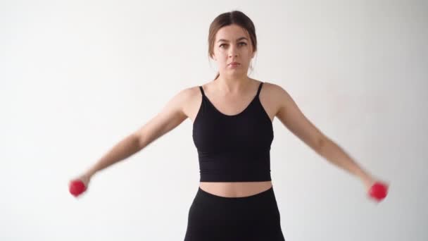 Vacker sexig tjej hemma tränar med hantlar. Övning för musklerna i armen ledningar till sidorna. vit vägg. — Stockvideo