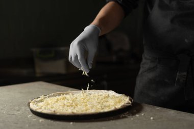 Eldivenli bir el serpintisi sert mozzarella peynirini yuvarlak bir çiğ pizzaya rendeledi. Diyetin için İtalyan pizzası pişirmek..