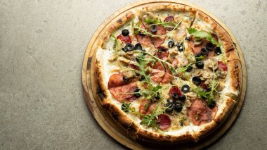 Hazır yuvarlak İtalyan pizzası peynirli, salamlı ve zeytinli gri arka planda yuvarlak ahşap bir tahta üzerinde. Metnin için yer.