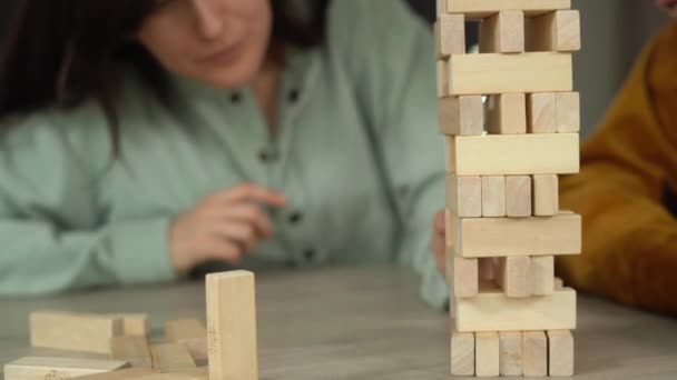 Voor de lol speelt een jong gezin thuis een spelletje houten blokjes. Het meisje trekt het blok uit zodat de toren op de tafel ligt.. — Stockvideo
