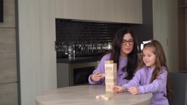 Ung brunett mamma bär glasögon spelar ett trä brädspel med sin lilla dotter 5 år gammal. Moderskap och barndomskoncept. — Stockvideo