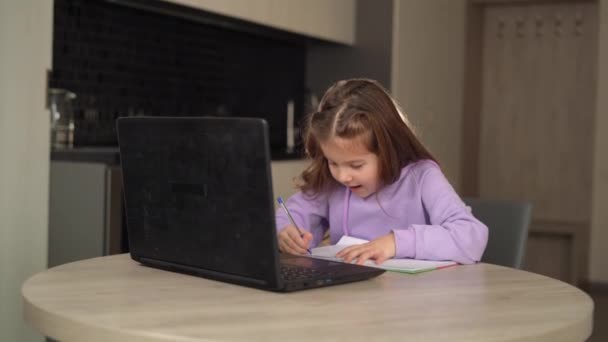 女子高生は執筆に忙しく、ノートパソコンを見てコロナウイルスに関する家庭教育を受けています-子供のeラーニングの概念、 covid-19パンデミックの間のバーチャル教室. — ストック動画