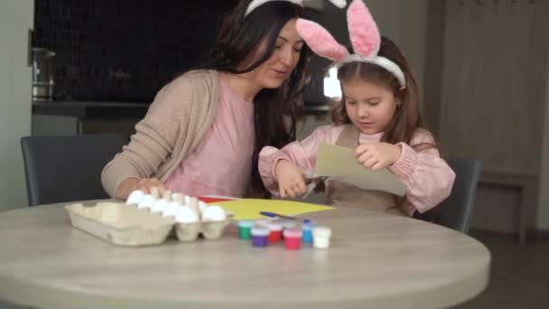 Feliz Pascua. Alegre familia se está preparando para las vacaciones de Pascua mamá y su hija con orejas de liebre recortar la forma de un conejo. — Vídeos de Stock