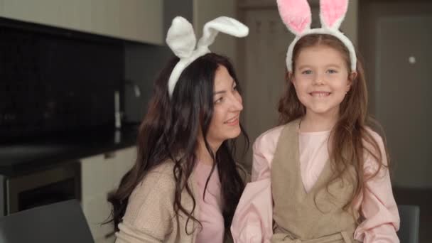 Mamma e figlia vestite con le orecchie di lepre sono seduti a casa. effettuare una videochiamata, chattare e guardare la fotocamera. concetto di pasqua felice durante la quarantena — Video Stock