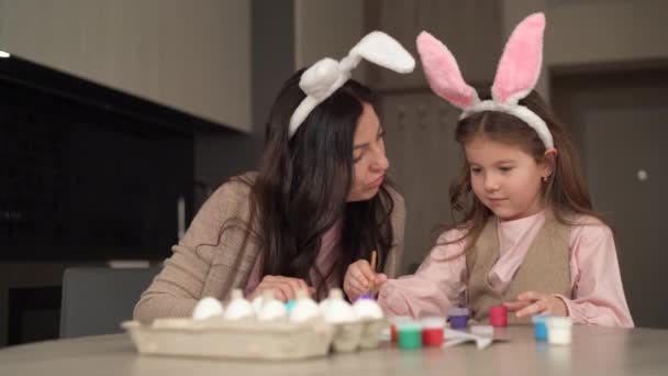 Feliz Pascua. Una familia alegre se está preparando para las vacaciones de Pascua. Mamá y su hija pintan huevos, juegan con pinturas. Se sientan en casa — Vídeos de Stock