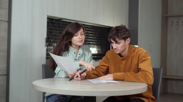 한 남자와 한 백인 여성 이 부엌에 앉아 있습니다. 종이 문서를 주의 깊이 작성 한다. . — 비디오
